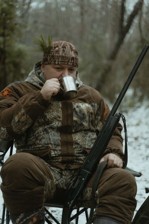 Free Man in camouflage enjoying a hot drink while hunting in the snowy woods. Stock Photo