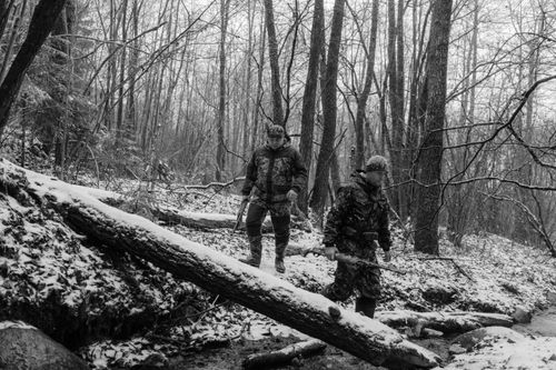 Free Two hunters in camouflage walking through a snowy forest, holding rifles. A monochrome winter scene. Stock Photo
