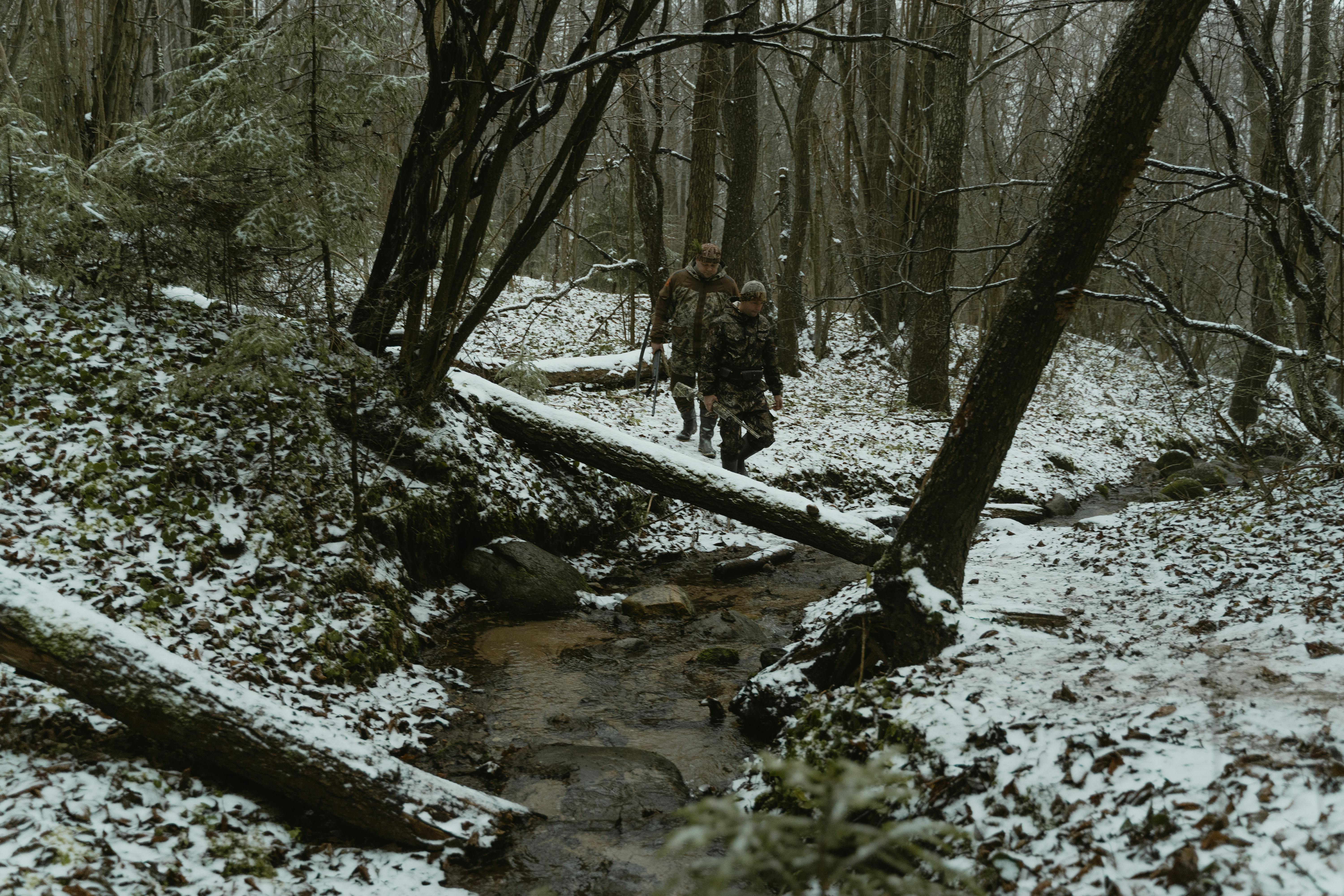 two men walking in the woods holding rifles