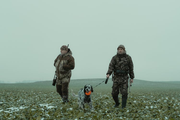 Two Men Walking In A Field With A Dog