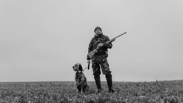 A hunter and his dog stand in a field in grayscale, creating a classic look.