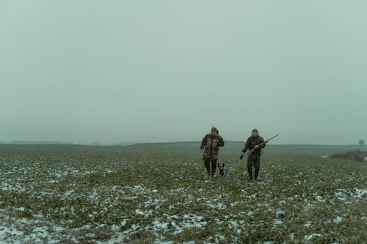 Two hunters with rifles and a dog in snowy countryside, exploring the winter landscape.