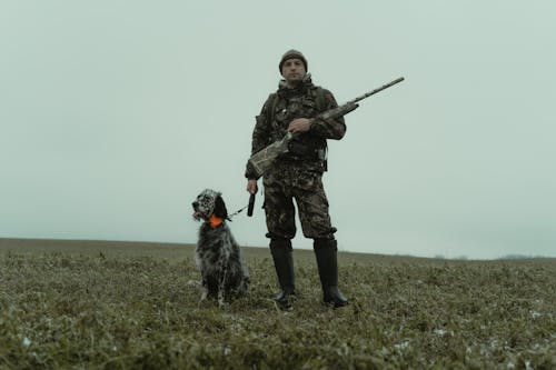 Man Holding a Rifle Standing beside a Pet Dog