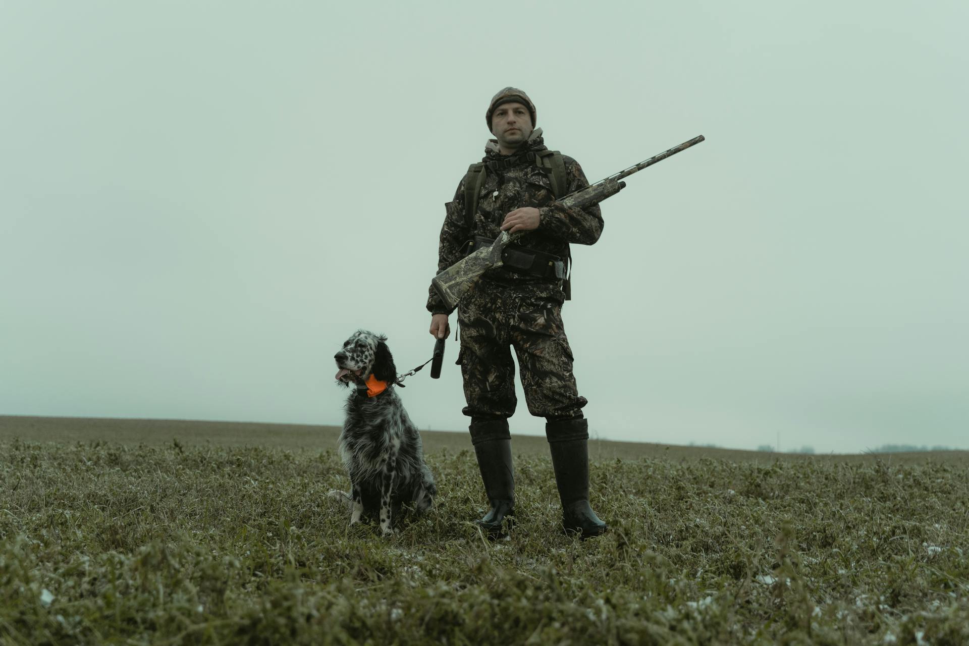 Man Holding a Rifle Standing beside a Pet Dog