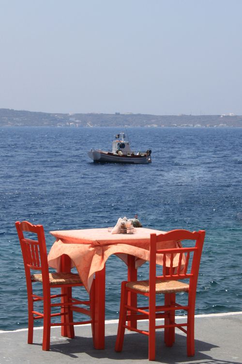 Free Red chairs and table set by the ocean, boat in the distance under sunny skies. Stock Photo