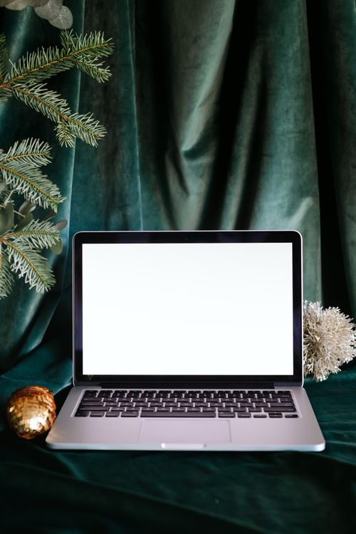 Free Elegant laptop mockup with a blank screen set against luxurious green fabric, accented by festive decorations. Stock Photo