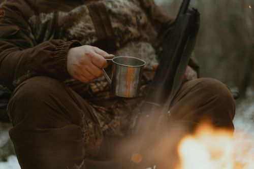 Free A person in camouflage enjoys a campfire with a tin cup outdoors. Stock Photo