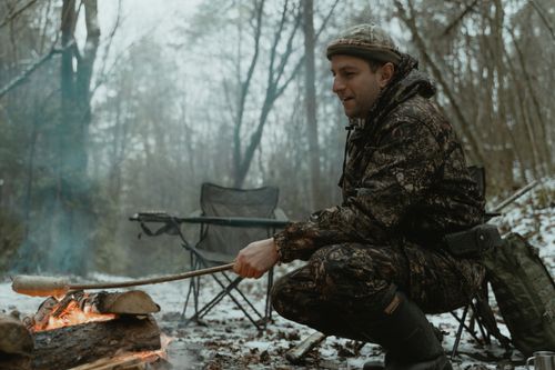 Free Man roasting food at a campfire in snowy forest, capturing winter adventure spirit. Stock Photo