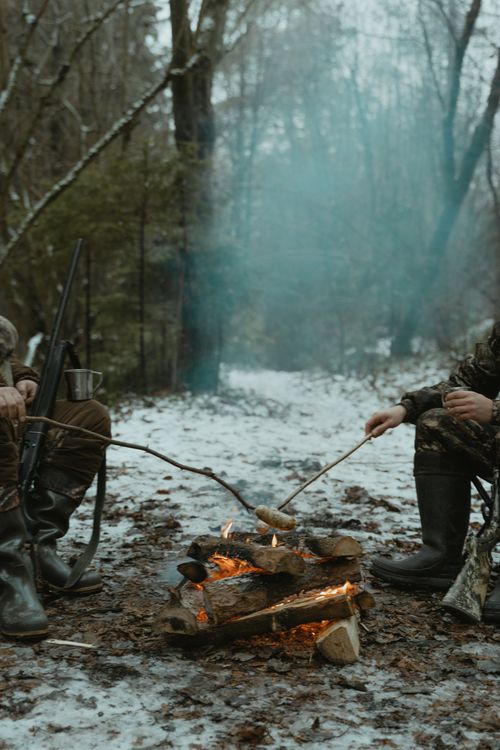 Free Two hunters roasting marshmallows near a campfire in a snowy forest. Stock Photo