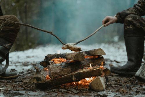 Free Two people roasting food over a campfire in a winter forest setting. Stock Photo