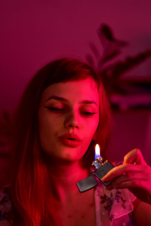 Free Serious female with long hair blowing out burning lighter with flame while sitting in obscure room with glowing red light at home Stock Photo