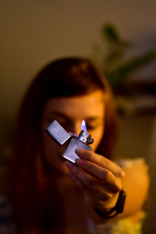 Free Anonymous blurred female with long hair showing burning lighter with warm flame in hand while sitting in room with yellow illumination Stock Photo