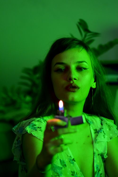 Free Concentrated female with burning lighter with hot flame in hand sitting in obscure room with glowing green light at home Stock Photo