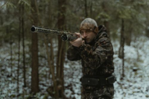 Free Hunter in camouflage aiming a rifle in a snowy forest, focusing intently on a target. Stock Photo