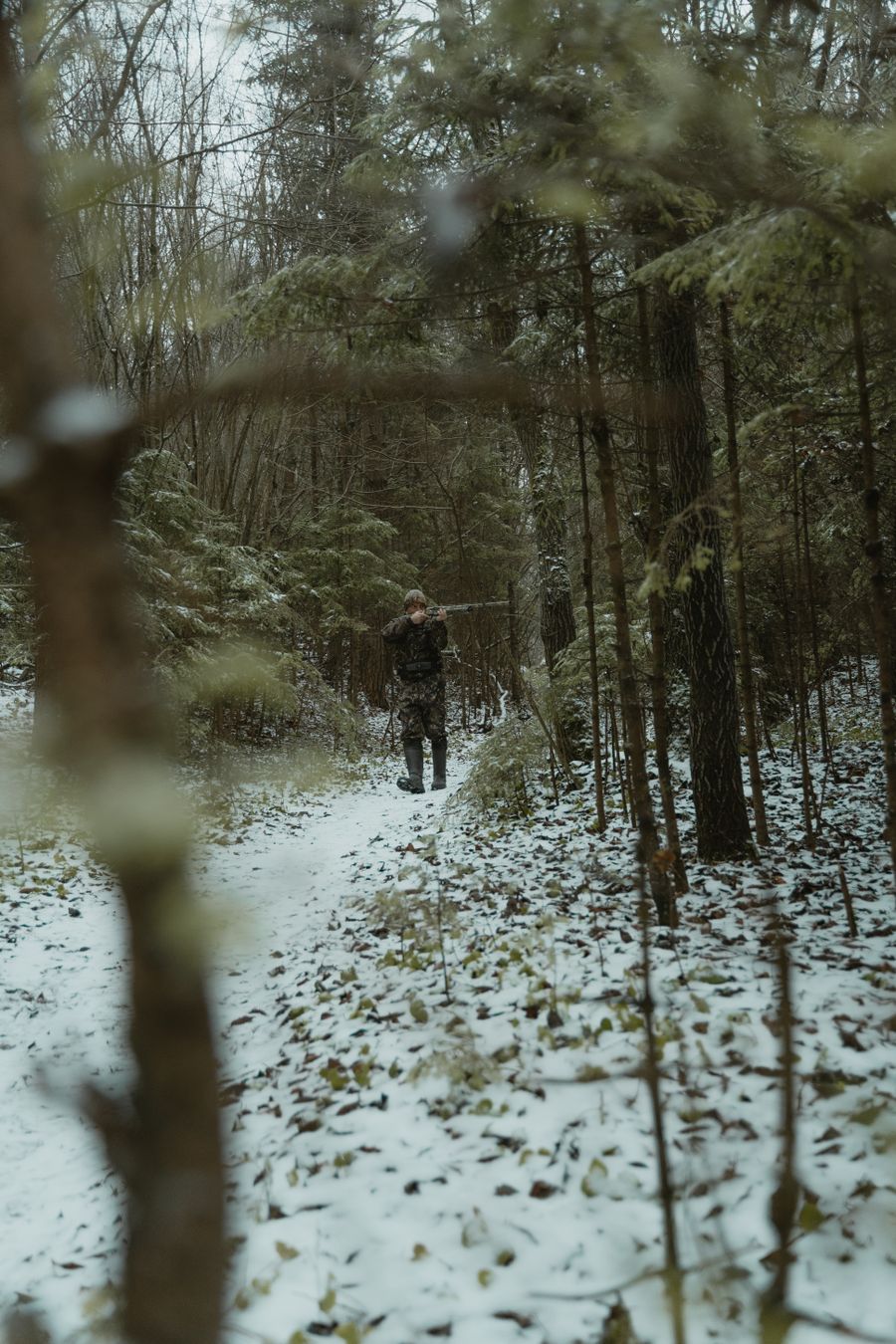 Deer hunter in camo aiming a rifle in the woods