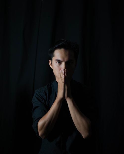Free A thoughtful man poses with a prayer gesture against a dark background. Stock Photo