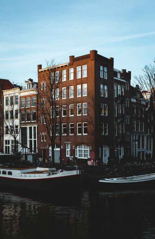 Free Exterior of aged red residential houses located on canal with moored boats and leafless trees in European city at daytime Stock Photo
