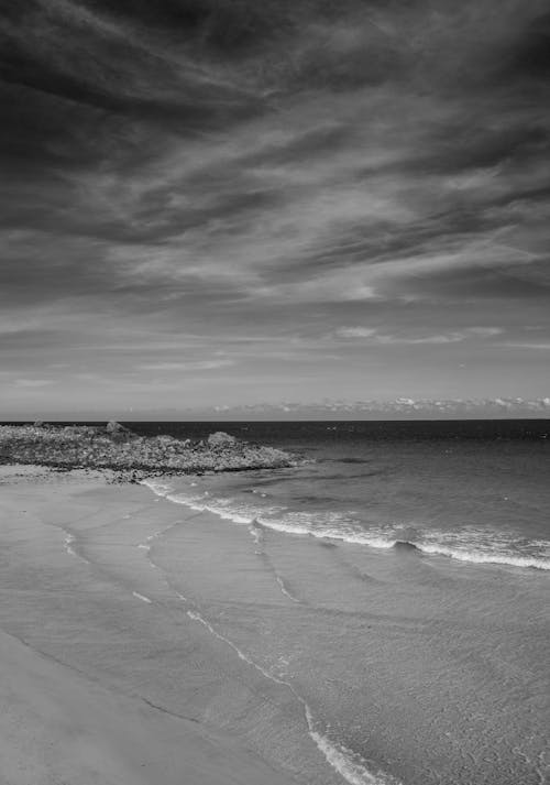 A Grayscale Photo of a Beach Under the Cloudy Sky