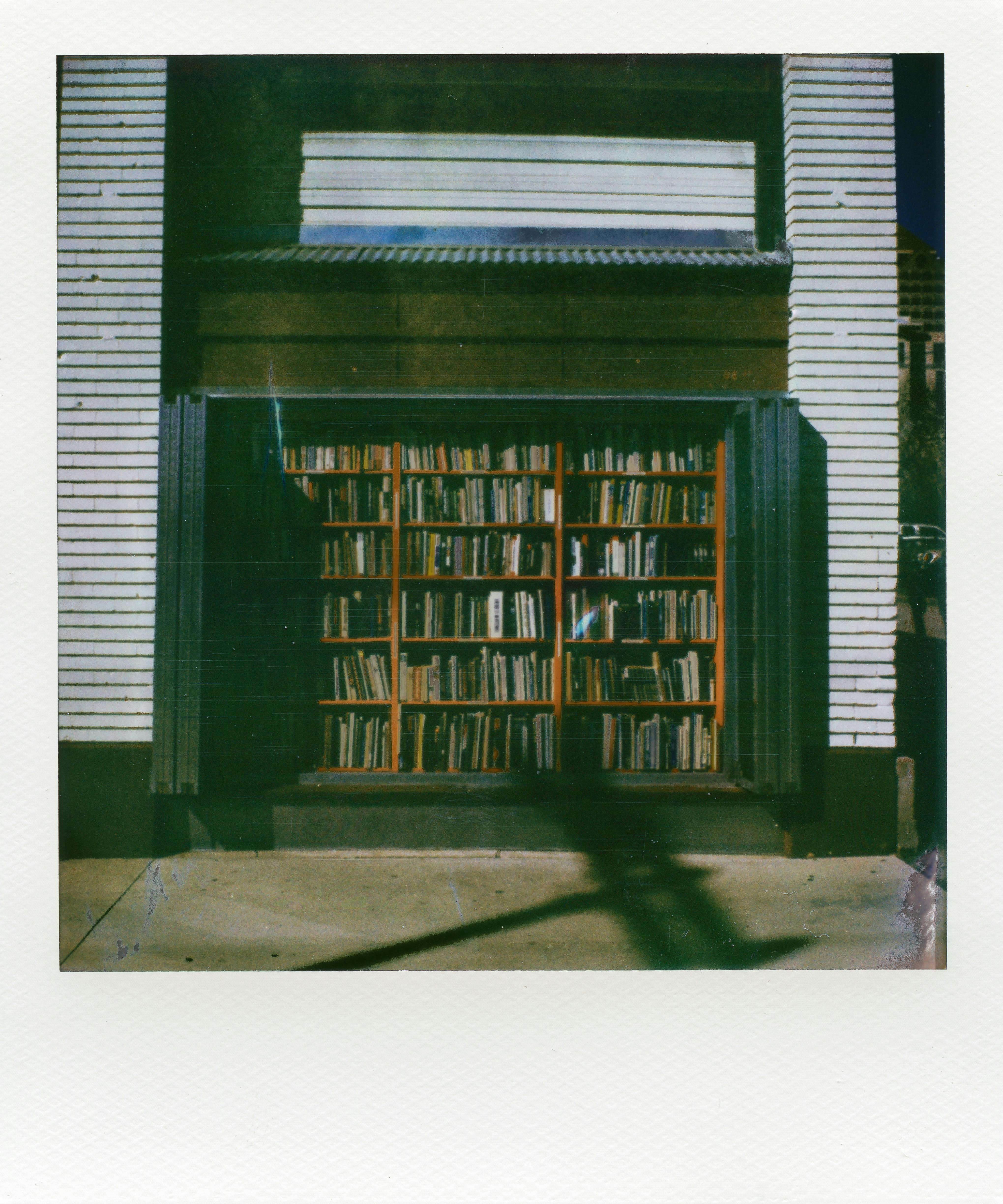A sunlit window display of books on a sidewalk, creating a vintage feel.