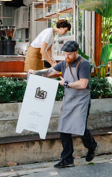 Employees setting up an outdoor sign at a modern cafe on a sunny day.