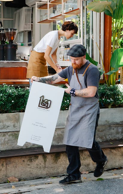 Photo by Tim Douglas Employees setting up an outdoor sign at a modern cafe on a sunny day.