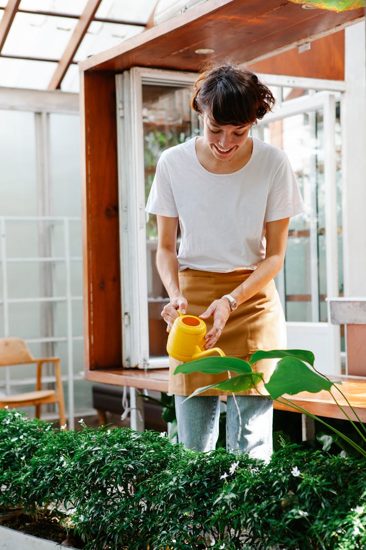 Female Employee Watering Plants In Greenhouse