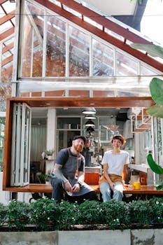 Two happy baristas sitting outside a modern café, enjoying a break on a sunny day.