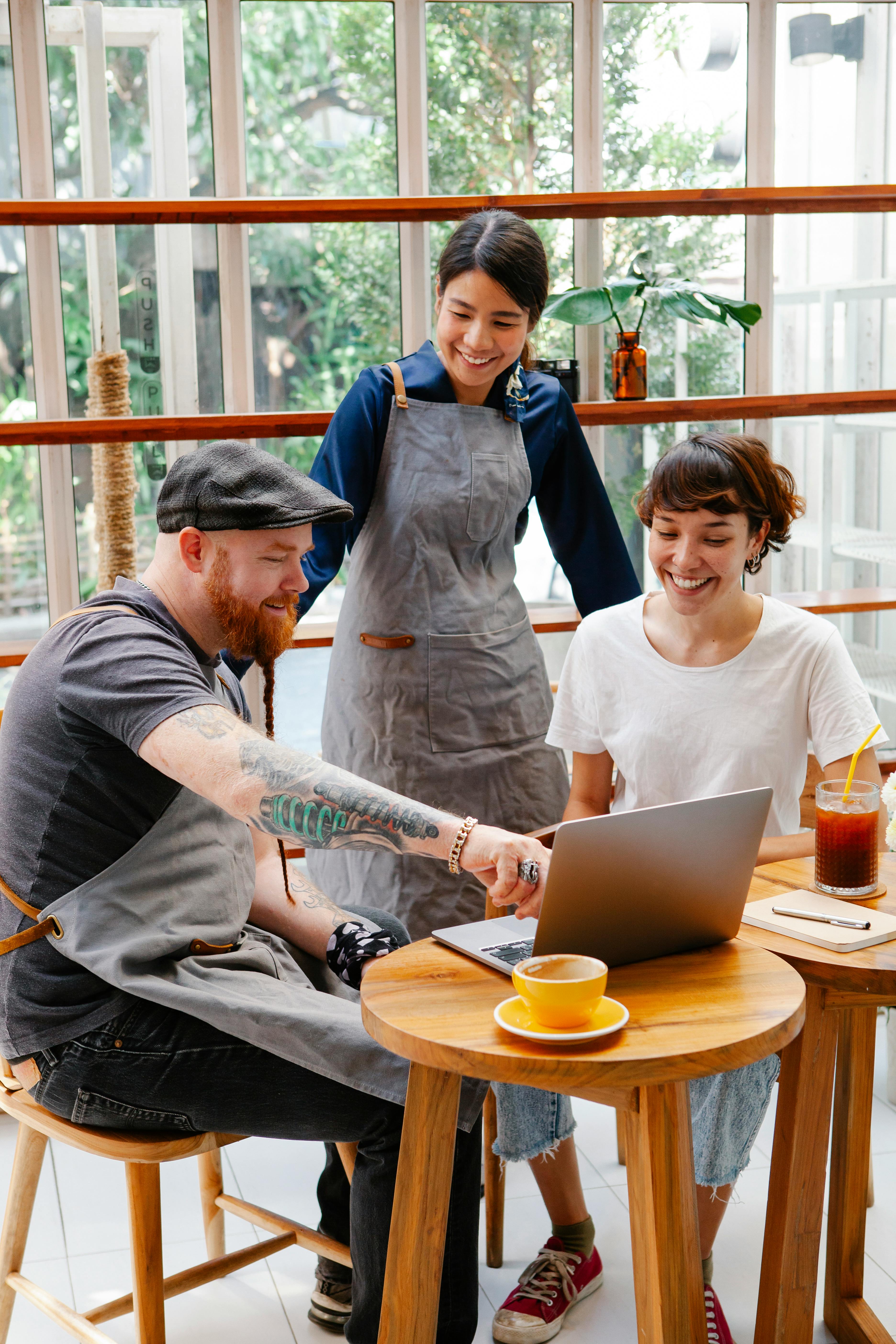 smiling multiracial cafe employees sharing laptop at work