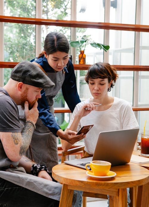 Diverse colleagues with smartphone and laptop speaking in cafe