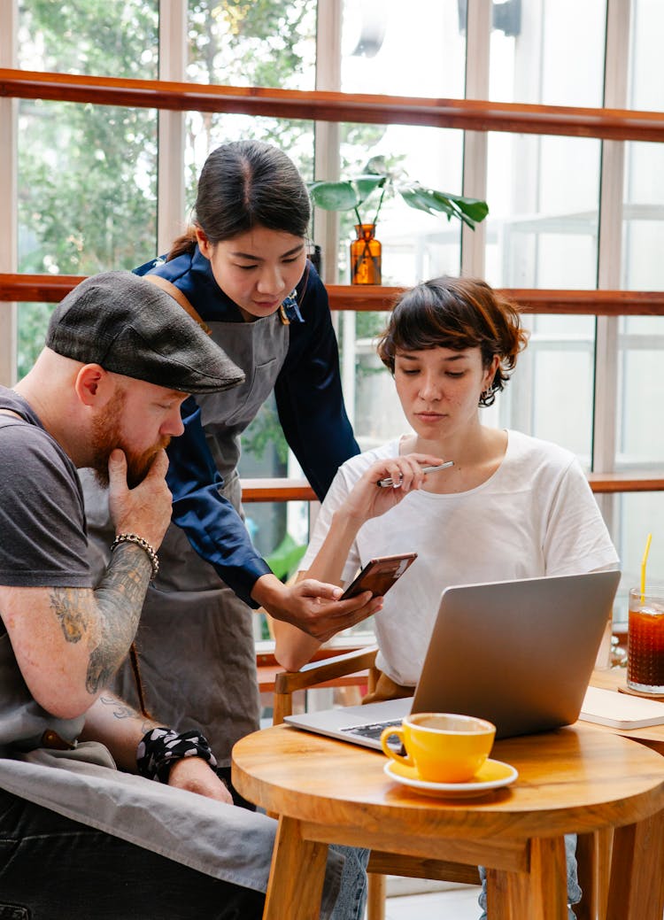 Diverse Colleagues With Smartphone And Laptop Speaking In Cafe