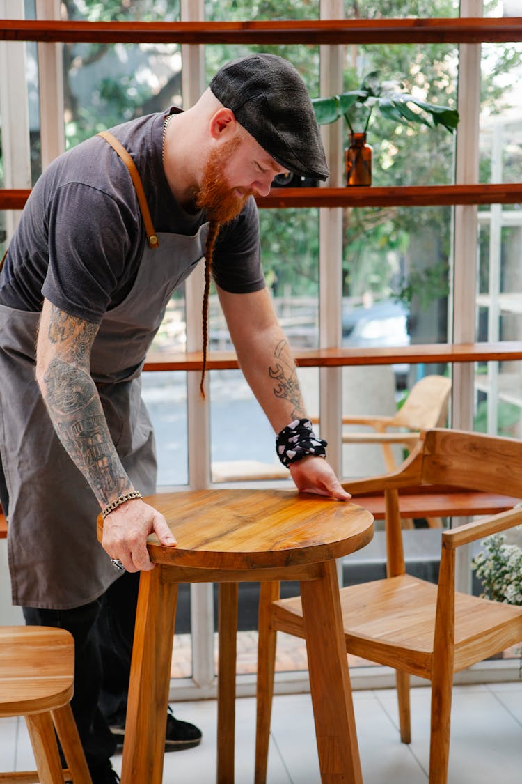 Smiling Hipster Cafe Employee Putting Table On Floor