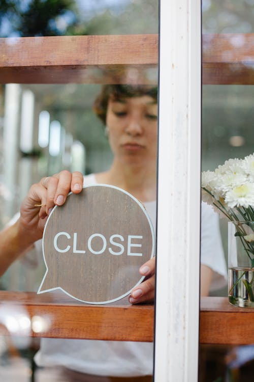 Free Through glass wall view of crop young cafeteria employee putting signboard with Close title on wooden beam Stock Photo