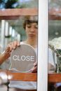 Through glass wall view of crop young cafeteria employee putting signboard with Close title on wooden beam