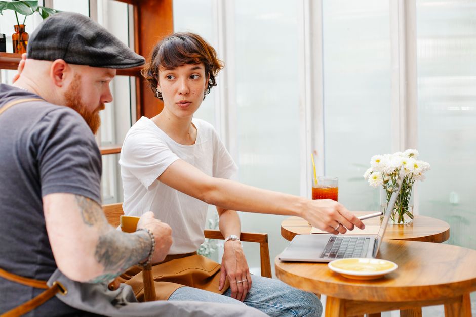 Deux personnes en pleine conversation autour d'un ordinateur portable dans un café