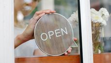 Through glass wall view of crop anonymous female cafeteria employee putting dialogue shaped signboard with Open title on wooden beam