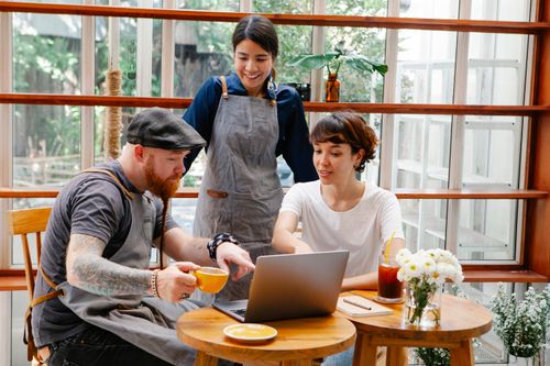 Free Smiling young multiracial coworkers with coffee using netbook while speaking at table in cafe Stock Photo