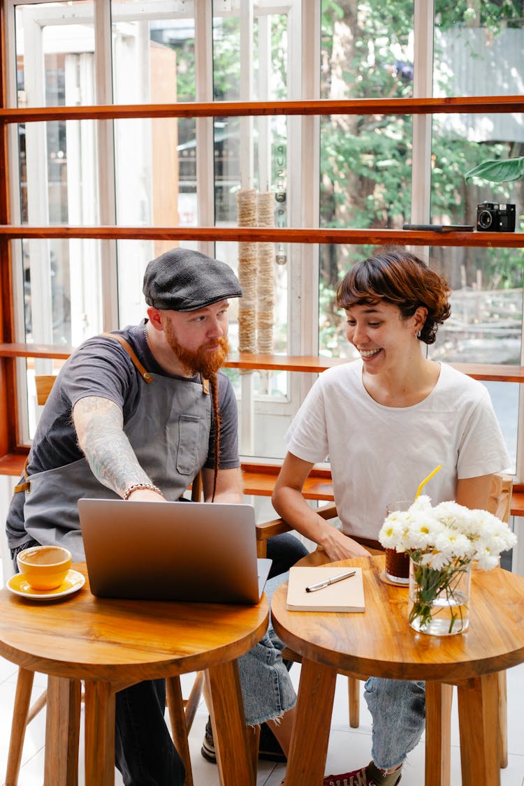 Content Barista Speaking With Hipster Partner Against Laptop In Cafe