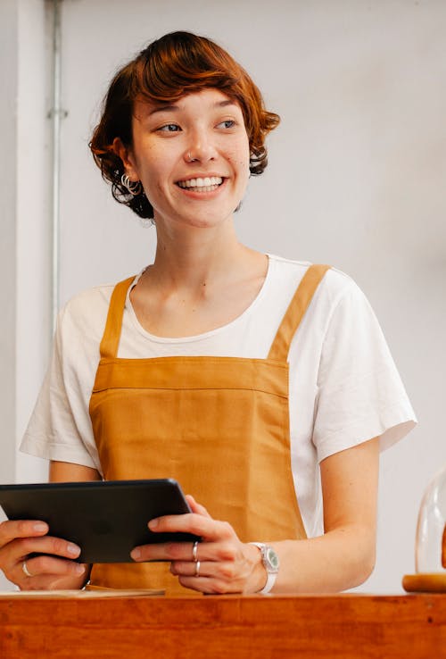 Free Young glad female employee with tablet looking away at counter in cafeteria in daylight Stock Photo