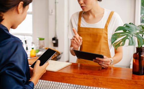Free Crop anonymous female employee with finger up speaking with partner touching black screen on cellphone in cafe Stock Photo