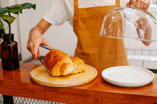 Free Crop anonymous female employee in apron putting tasty pastries with tongs on plate in bakery Stock Photo
