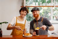 Content coworkers showing tasty pastry and Black Velvet cocktail while looking at camera at counter