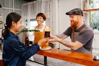 Glad hipster male employee passing glass of Black Velvet cocktail to smiling ethnic colleague at work