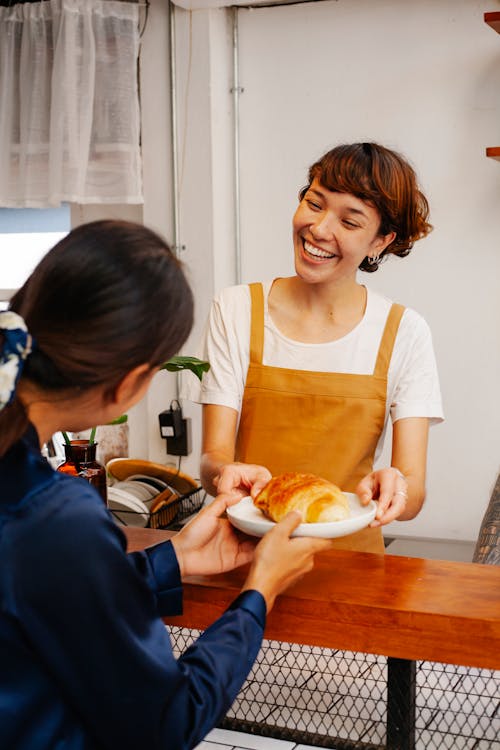 Content baker passing delicious pastry to unrecognizable coworker at counter