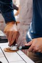 Crop anonymous male employee pressing coffee in portafilter with tamper on table in cafeteria