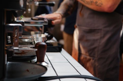 Free Side view of crop unrecognizable tattooed male worker cleaning electric coffee machine with rag in cafeteria Stock Photo