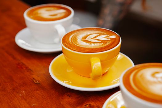 Bright ceramic saucers and cups with tasty coffee with ornament on smooth froth on cafe counter