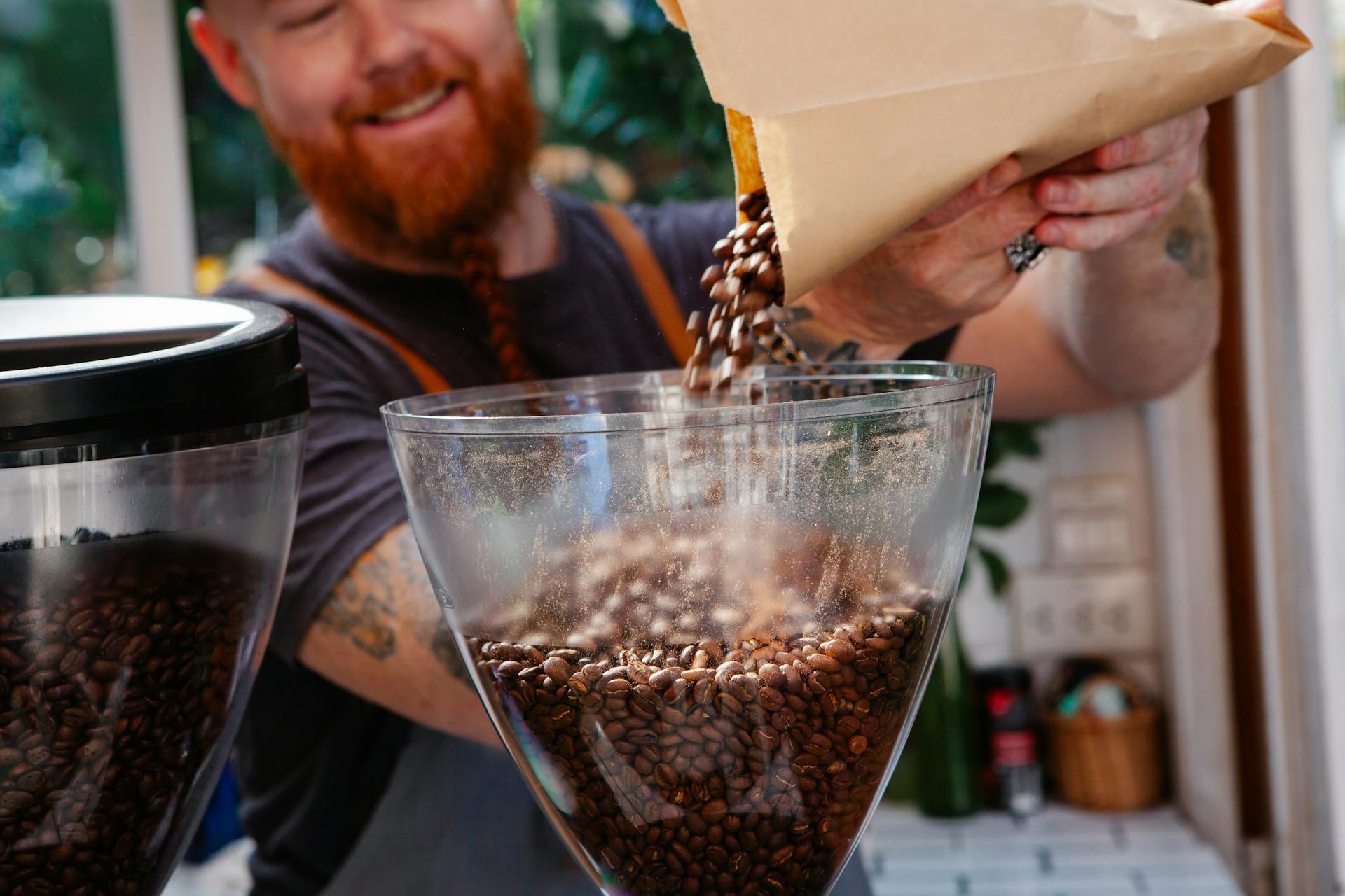 Crop content hipster employee pouring coffee beans into grinder