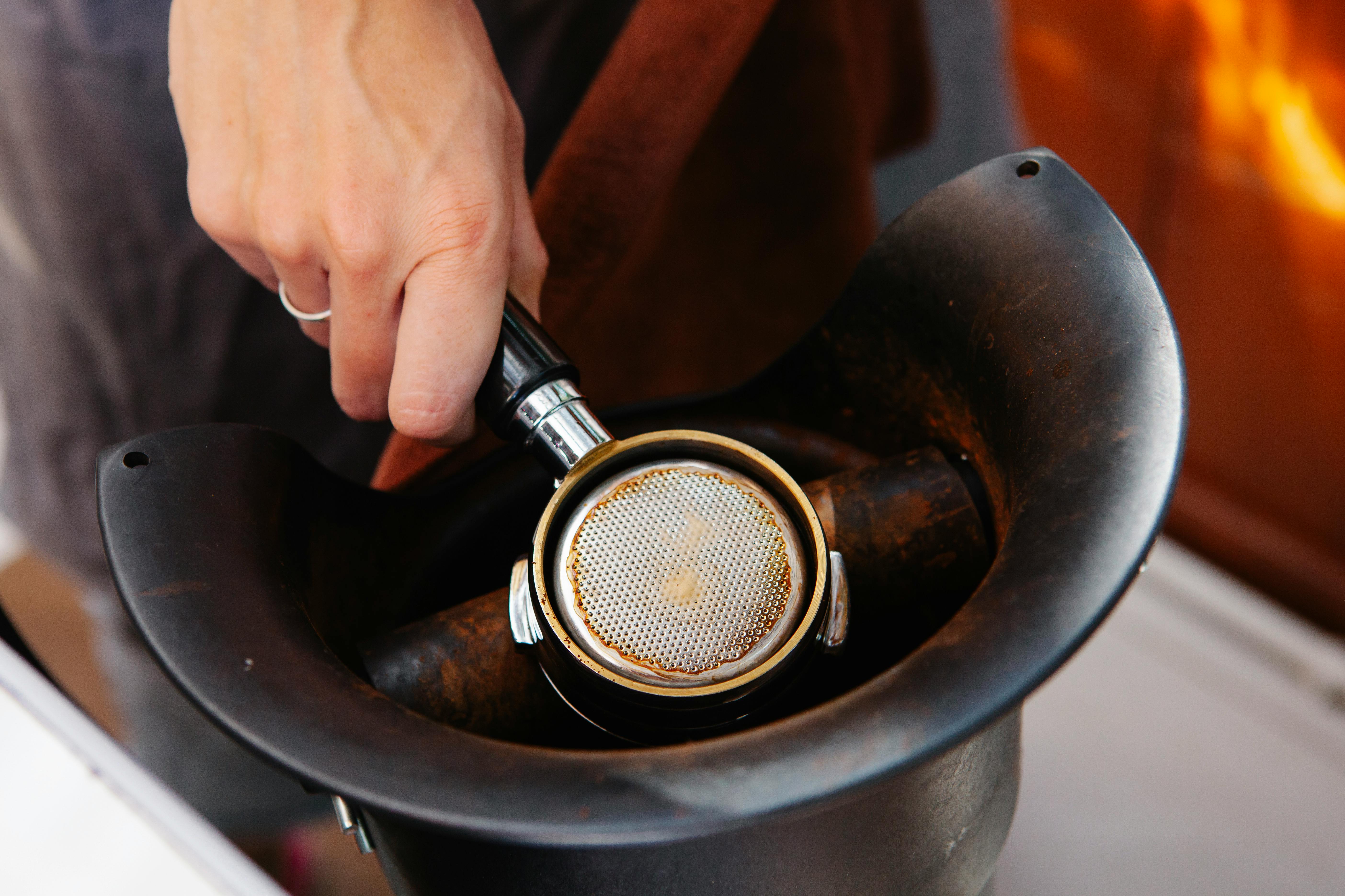 crop barista with portafilter in coffee grinder in cafeteria