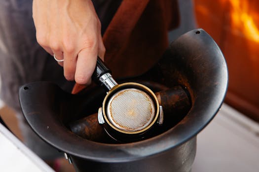 From above of faceless female employee with metal portafilter in electric coffee grinder in cafe