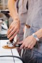 Crop anonymous female employee pressing coffee in metal portafilter with tamper near partner in cafeteria